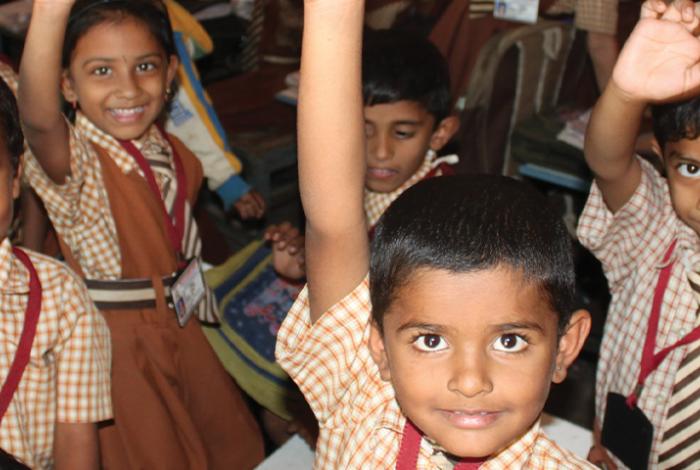 photo, Indian children in classroom smile with raised hands and waving