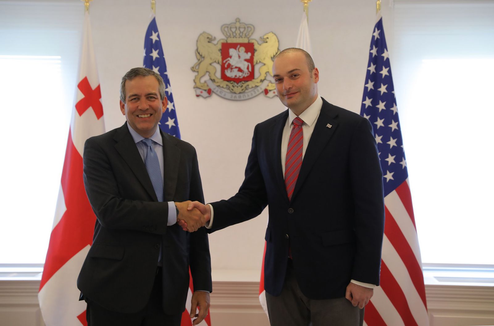 Photo of OPIC Executive Vice President David Bohigian shaking hands with Georgian Prime Minister Mamuka Bakhtadze standing in front of USA and Georgian flags, OPIC, Overseas Private Investment Corporation, Republic of Georgia, David Bohigian, Mamuka Bakhtadze, investment, Caucasus, Anakali, Poti, infrastructure, development finance, investing overseas