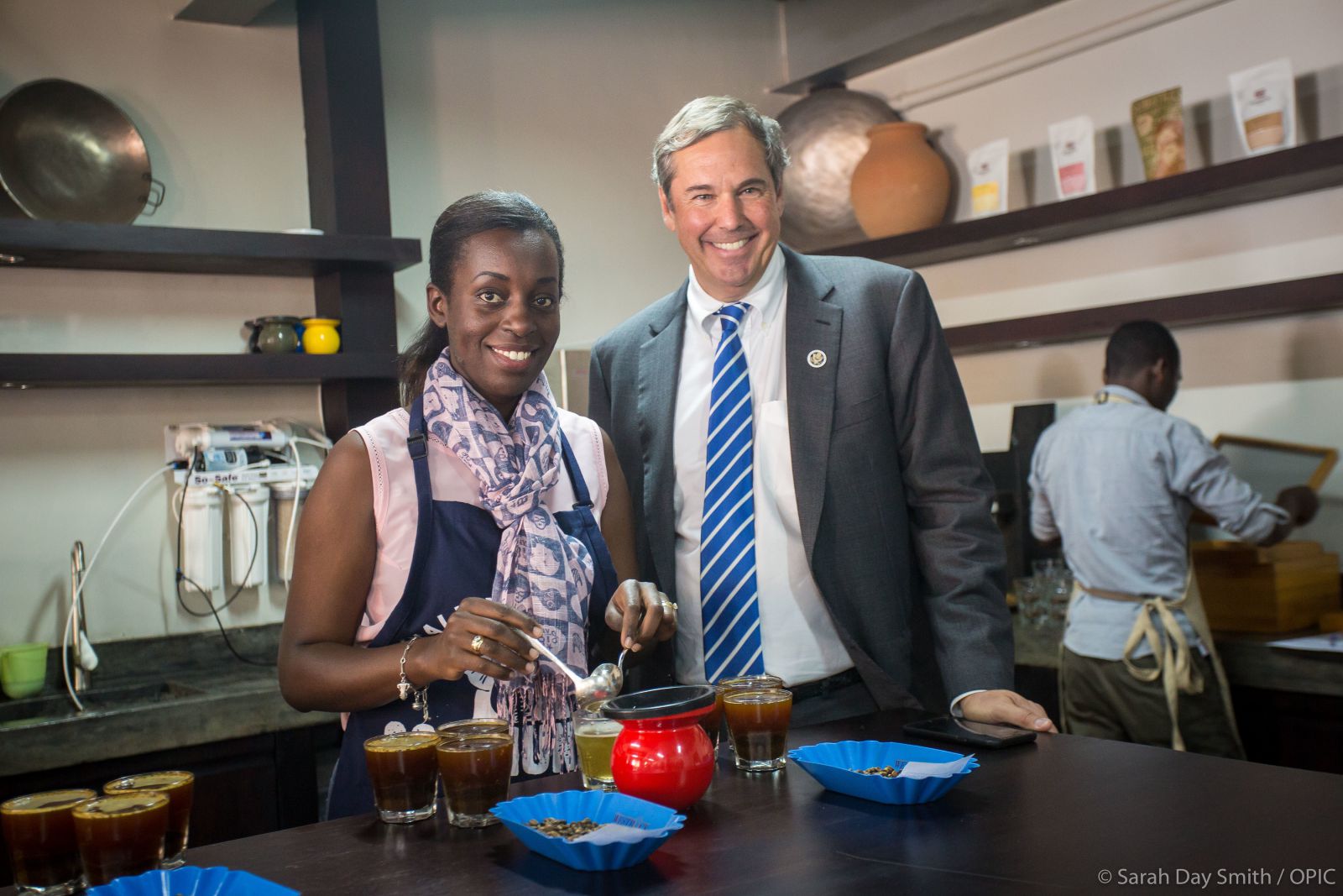 OPIC President and CEO Ray W Washburne visits Rwanda Trading Company, standing with woman in test kitchen; Overseas Private Investment Corporation, development finance