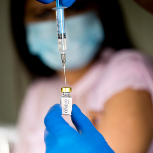 COVID-19 vaccine dose in front of a masked woman